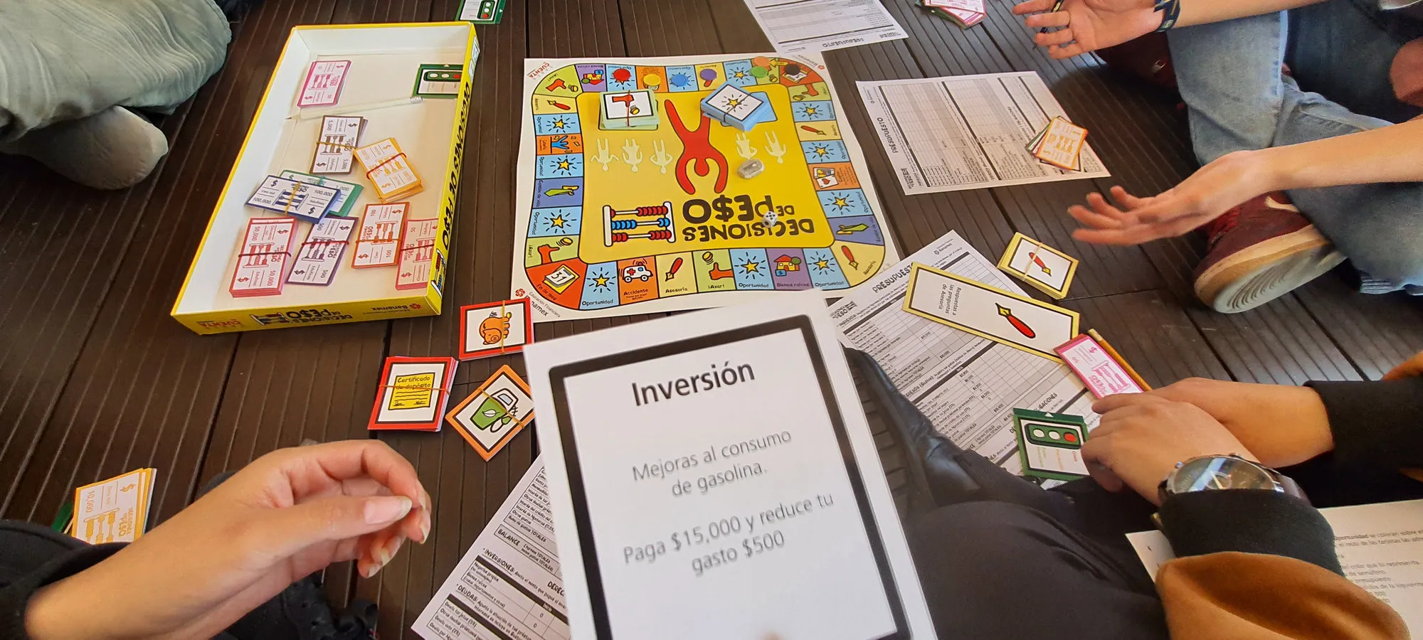 Mesa de juego “Decisiones de peso” con billetes de práctica, tarjetas de inversión y hojas de presupuesto